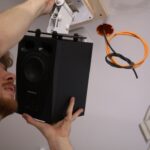 Montage der Deckenlautsprecher: Johannes Frank befestigt einen ADAM Audio A4V auf einer individuell angefertigten Holzhalterung. Die orangefarbenen Netzwerk- und Stromleitungen führen sternförmig zu jeder Position im Raum.